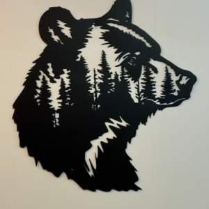 Black metal wall art shaped like a bear’s head with pine tree cutout details, mounted on a light wall.