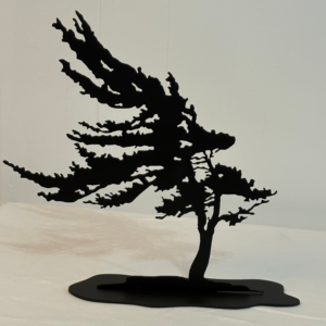 Freestanding black metal silhouette of a windblown tree leaning to one side on a wide flat base, displayed on a white table against a light wall.